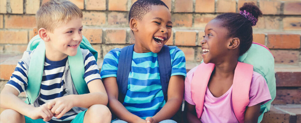 Three diverse kids sitting laughing enjoying life